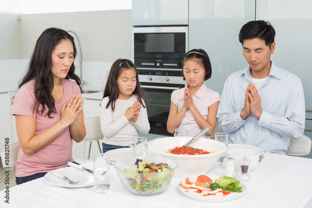 Family of four saying grace before meal in kitchen Family of four saying grace before meal in kitchen
