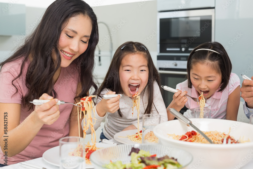 Woman with kids enjoying spaghetti lunch in kitchen