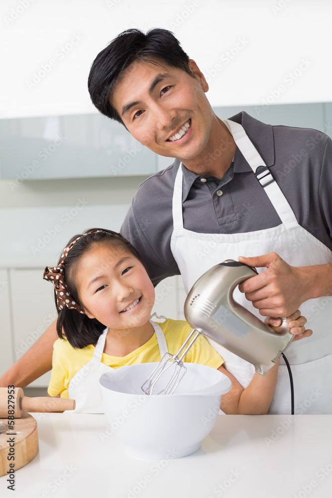 Man with his daughter using electric whisk into bowl in kitchen Man with his daughter using electric whisk into bowl in kitchen