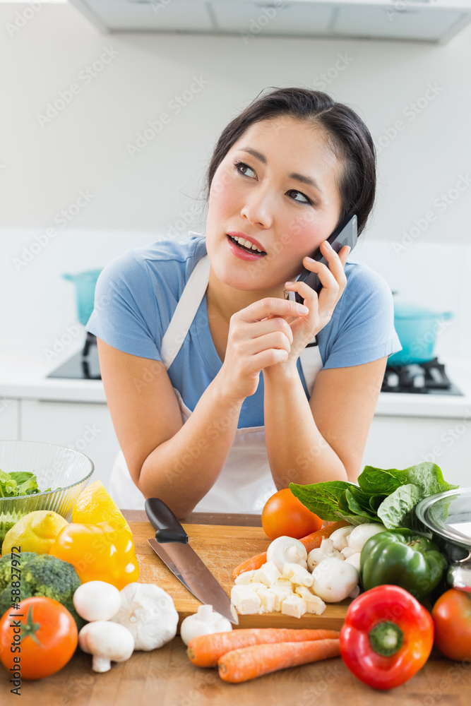 Woman using mobile phone in front of vegetables in kitchen Woman using mobile phone in front of vegetables in kitchen