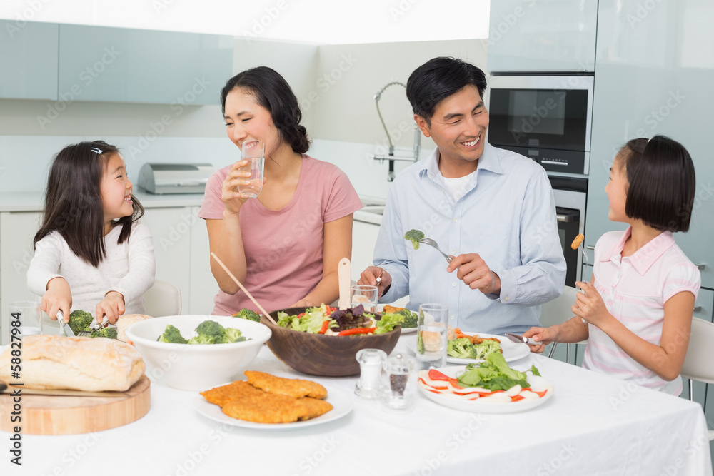 Young family of four enjoying healthy meal in kitchen Young family of four enjoying healthy meal in kitchen