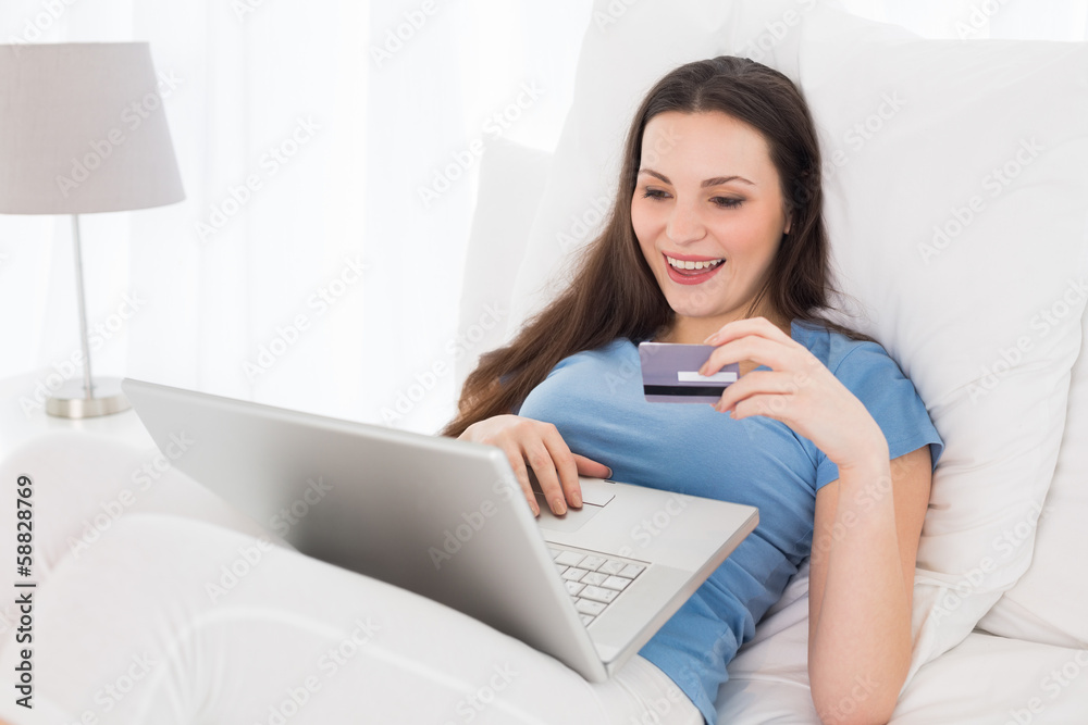 Cheerful casual woman doing online shopping in bed Cheerful casual woman doing online shopping in bed