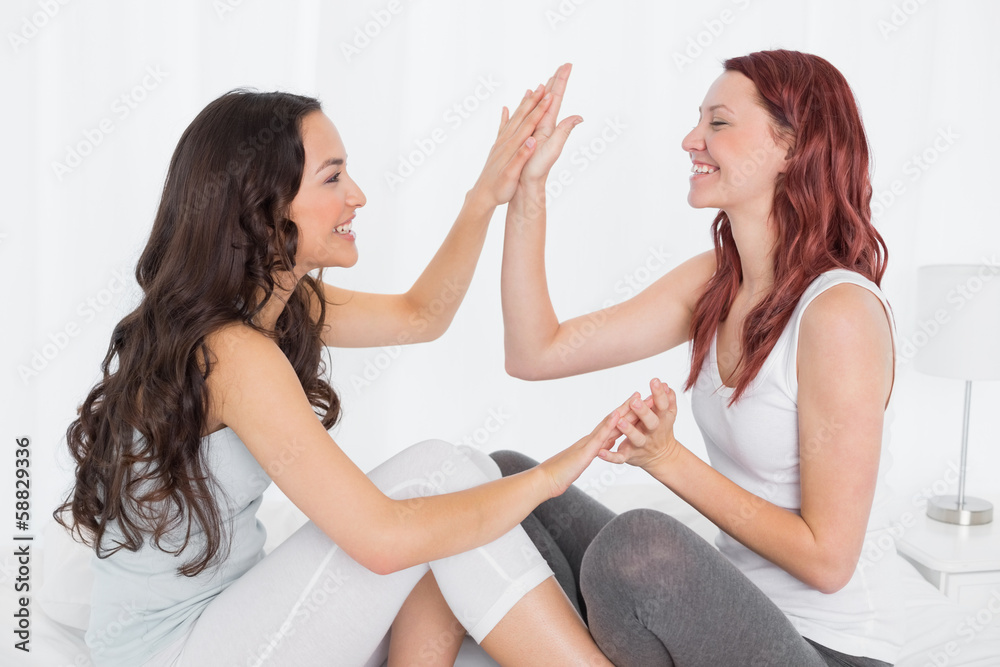 Happy female friends playing clapping game on bed Happy female friends playing clapping game on bed
