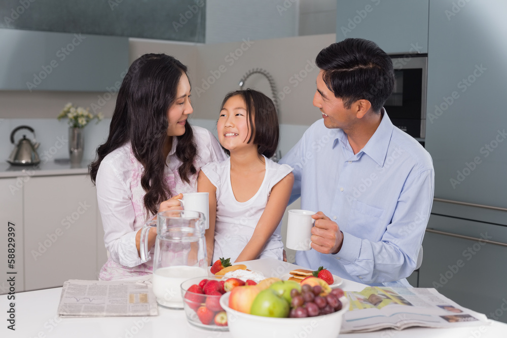 Happy young girl enjoying breakfast with parents Happy young girl enjoying breakfast with parents