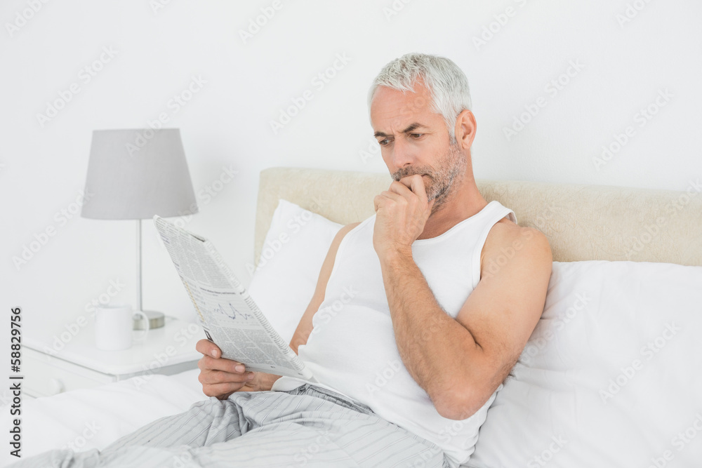 Mature man reading newspaper in bed at home Mature man reading newspaper in bed at home