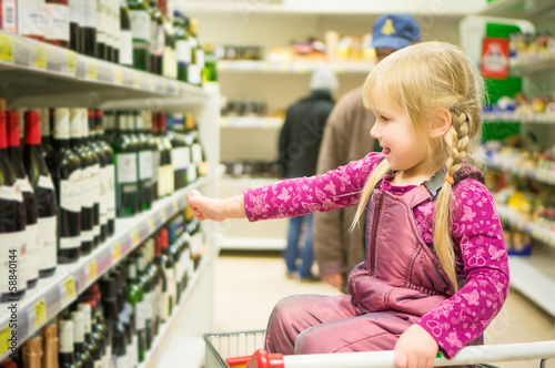 Adorable girl grimacing sitting in shopping cart in alcoholic be