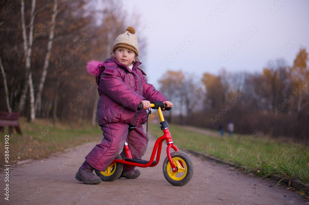 Adorable girl ride on learner bike in autumn park