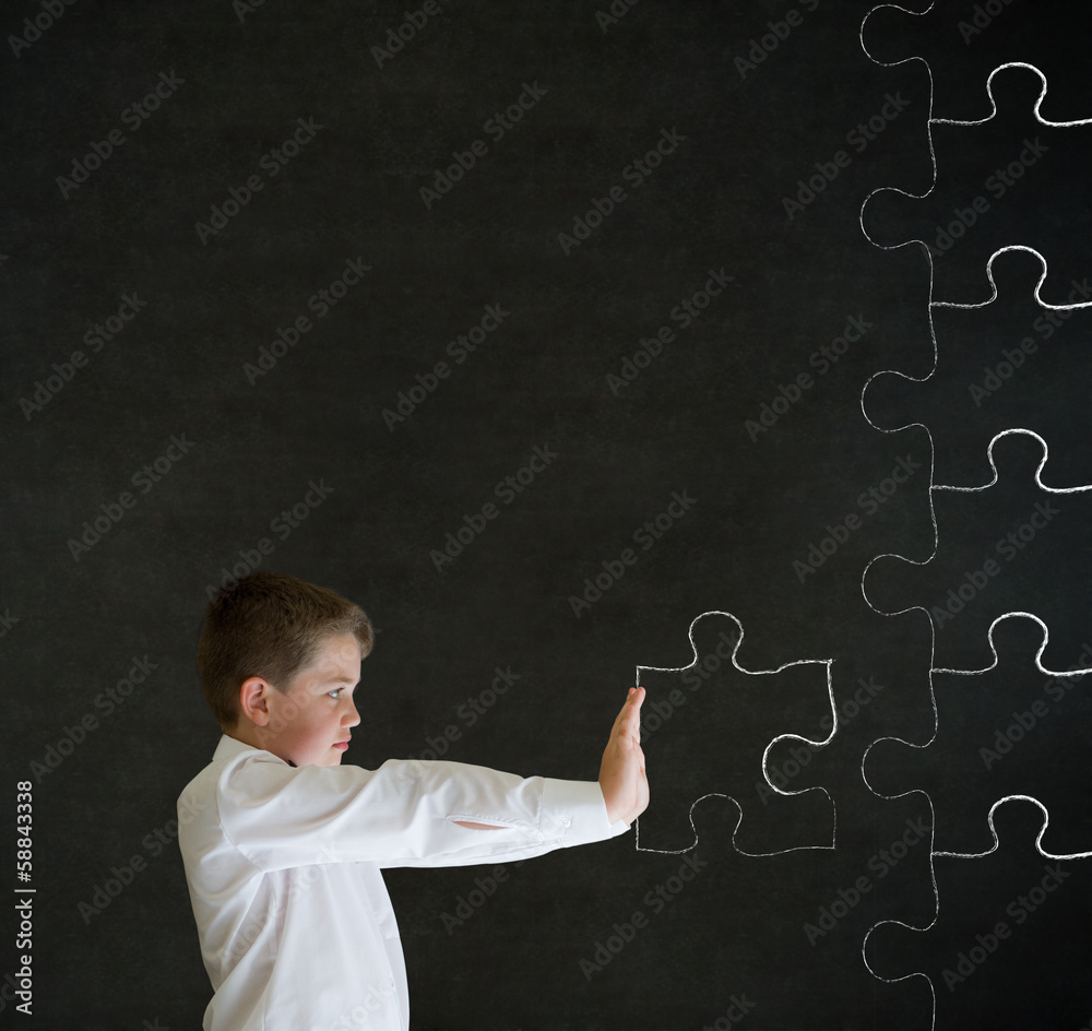 Boy pushing puzzle piece on blackboard background