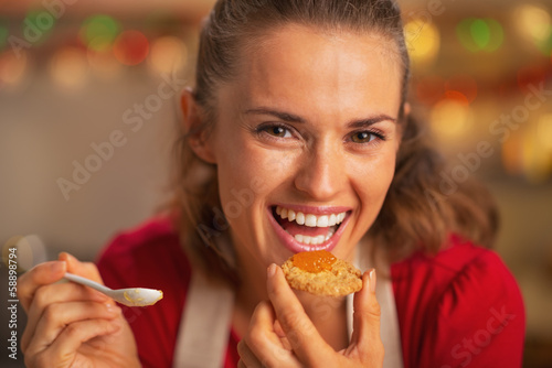 Portrait of smiling young housewife eating orange jam
