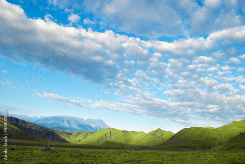 landscape of green meadow, mountain, blue sky and clouds, Russia
