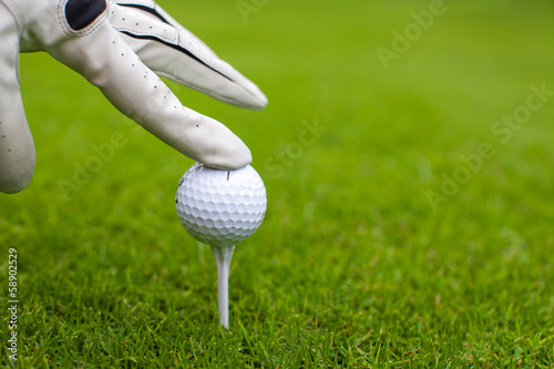 Hand placing golf-ball on tee over golf course with green grass