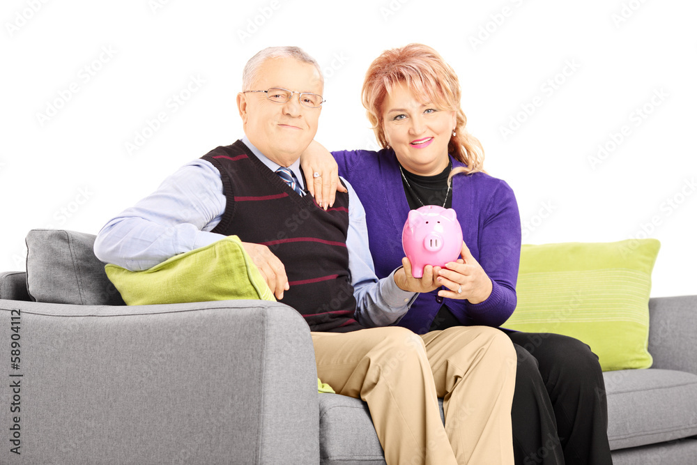 Mature couple sitting on a sofa and holding a piggy bank Mature couple sitting on a sofa and holding a piggy bank