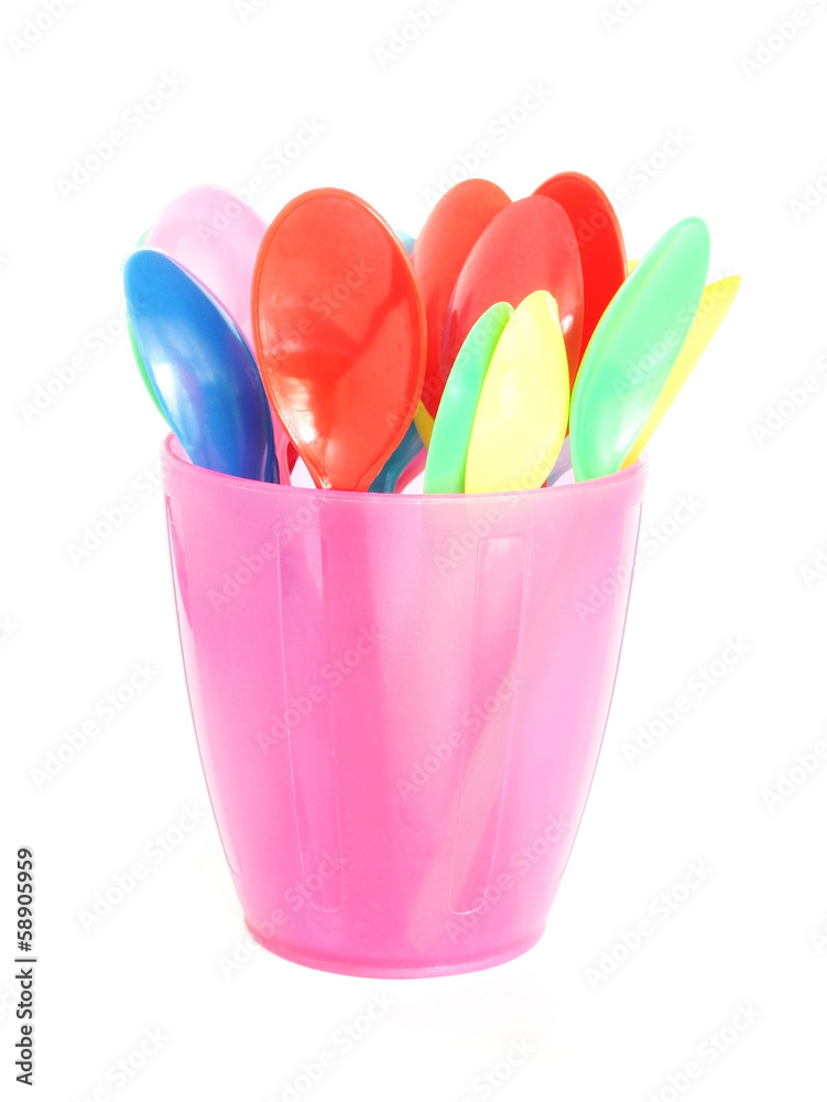 multicolor plastic spoons in pink glass on white background