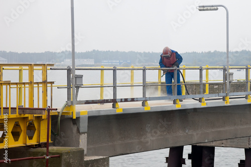Φωτογραφία Worker sandblasting barrier on the waterfront.