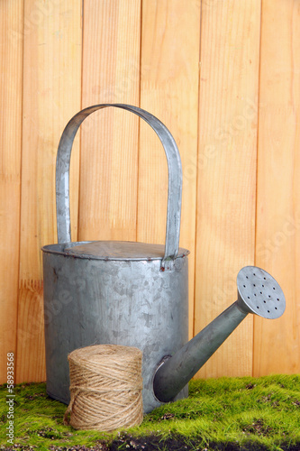 Watering can on grass on wooden background