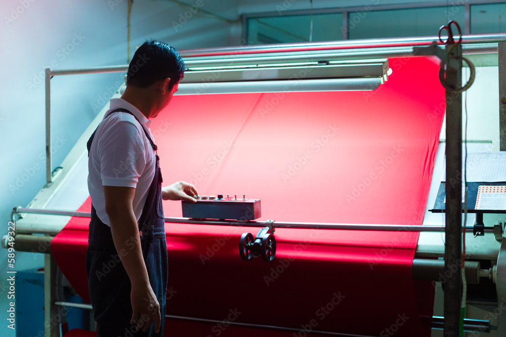 Asian worker controls fabrics in textile plant - obrazy, fototapety, plakaty 