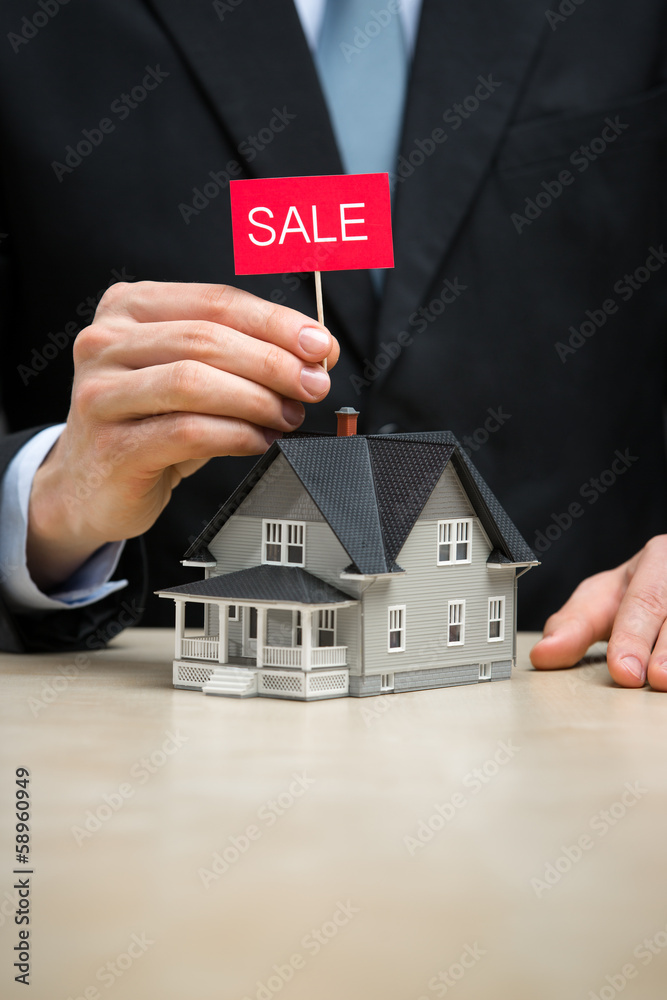 Close up of little house and hand keeping sale tablet Close up of little house and hand keeping sale tablet