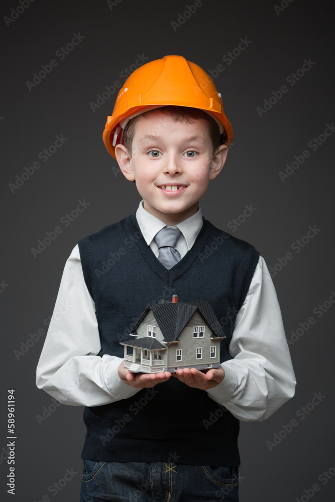 Portrait of boy in hard hat keeping house model on grey