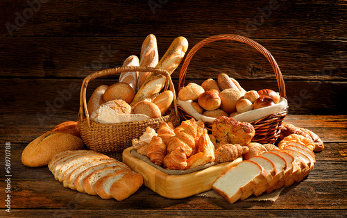 Valokuva Variety of bread in wicker basket on old wooden background.