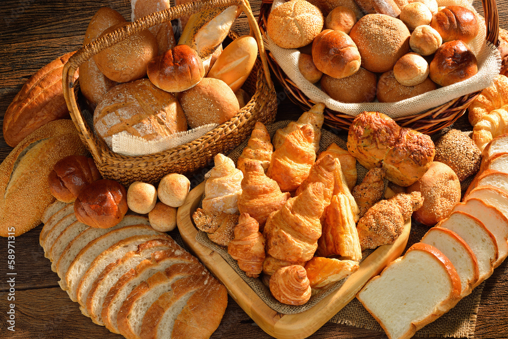 Variety of bread in wicker basket on old wooden background. - obrazy, fototapety, plakaty 