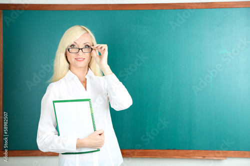 School teacher near blackboard with folder in classroom