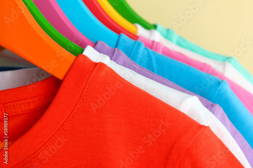 Different shirts on colorful hangers on beige background photo