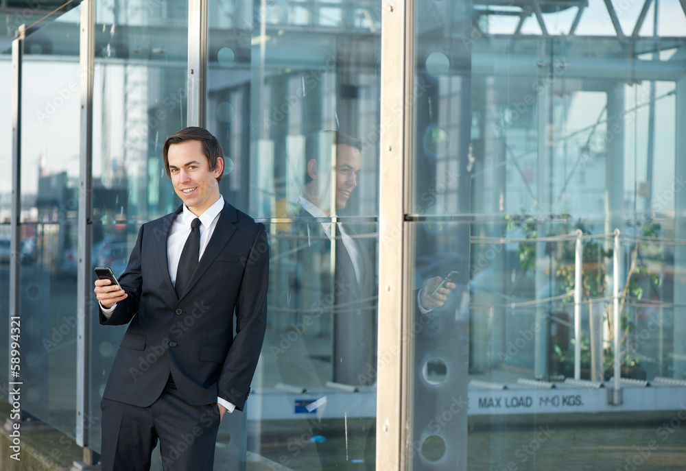 Young businessman standing outdoors with mobile phone
