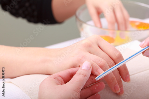 Beautician with file filing nails female client. Beauty salon