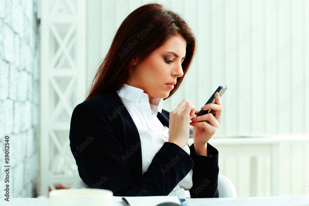 Young serious businesswoman typing on her smartphone in office Young serious businesswoman typing on her smartphone in office