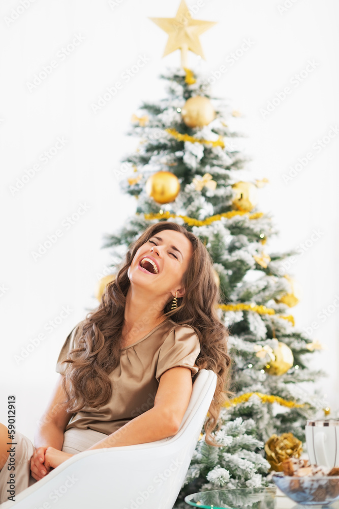 Portrait of young woman sitting near christmas tree and laughing