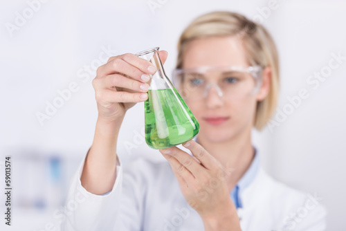 chemielaborantin schaut auf glaskolben mit flüssigkeit photo