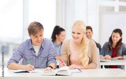 two teenagers with notebooks and book at school © Syda Productions