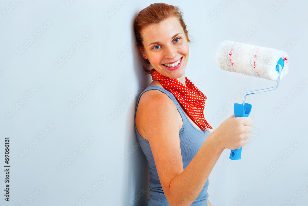Happy woman with roller brush standing against wall. Happy woman with roller brush standing against wall.