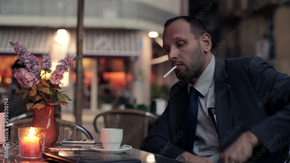 Young businessman smoking cigarette at the cafe
