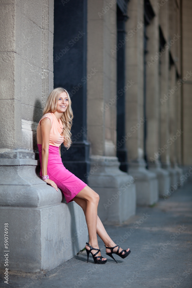 beautiful lady leans against columns in a dress.