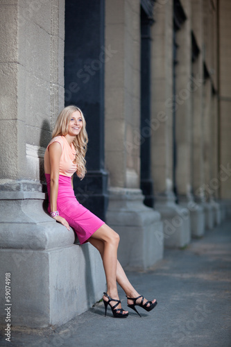 beautiful lady leans against columns in a dress.
