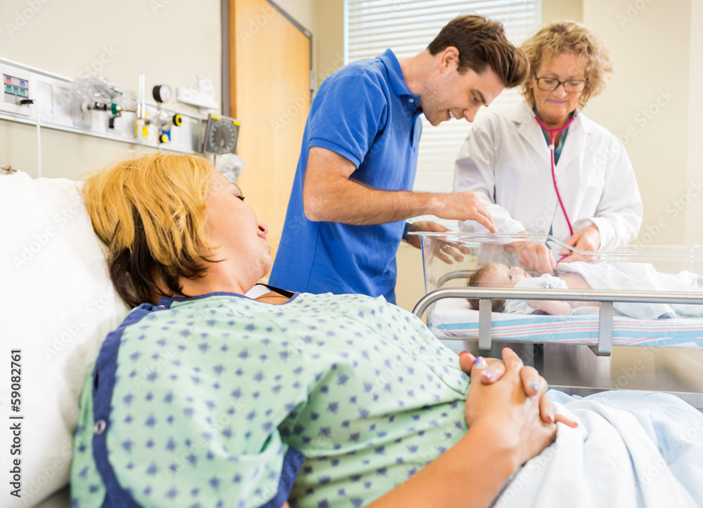 Mature Doctor Examining Newborn Babygirl While Parents Looking A Mature Doctor Examining Newborn Babygirl While Parents Looking A