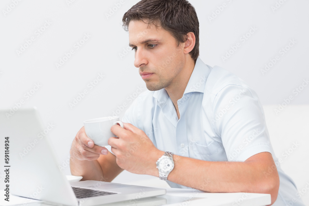 Serious man with teacup using laptop at home Serious man with teacup using laptop at home