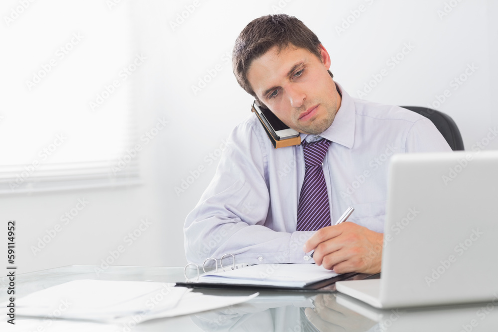 Businessman on call while writing in diary at office Businessman on call while writing in diary at office