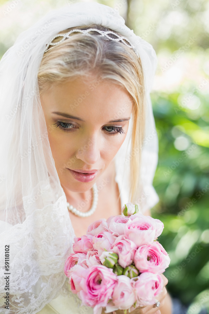 Obraz premium Smiling bride wearing veil holding bouquet looking down