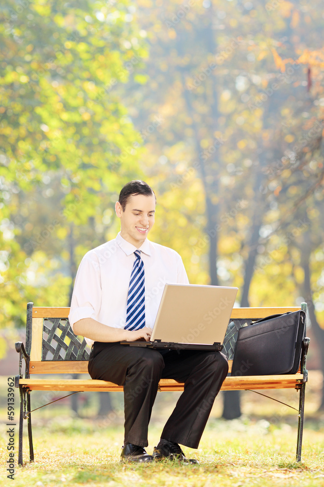 Young businessman sitting on a wooden bench working on a laptop Young businessman sitting on a wooden bench working on a laptop
