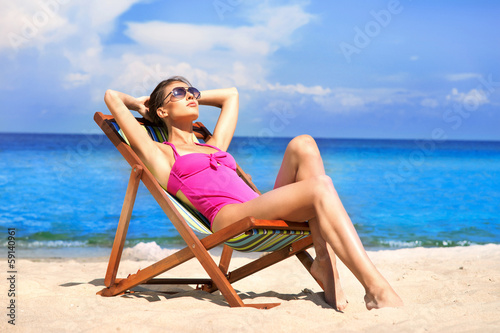 A young woman in a swimsuit relaxing on a deckchair on the beach © Acronym