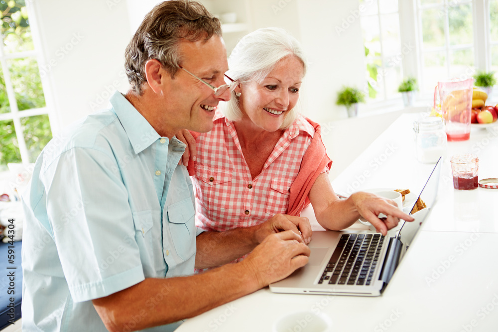 Middle Aged Couple Looking At Laptop Over Breakfast Middle Aged Couple Looking At Laptop Over Breakfast