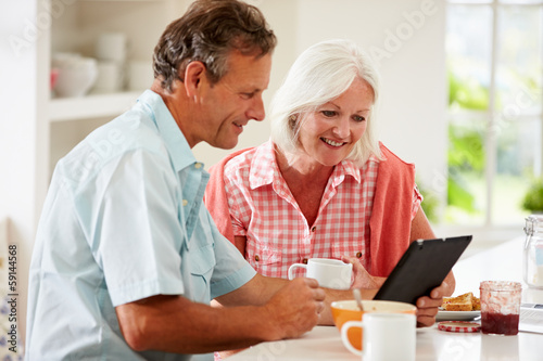 Middle Aged Couple Looking At Digital Tablet Over Breakfast
