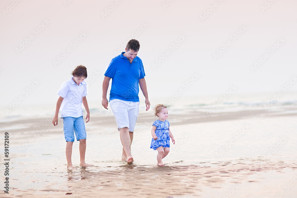 Young father with his son and toddler girl walking at the beach