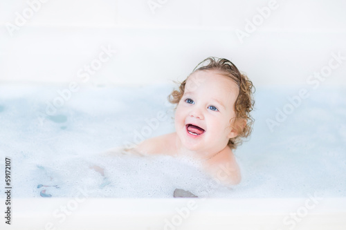 Funny toddler girl having a bath with foam