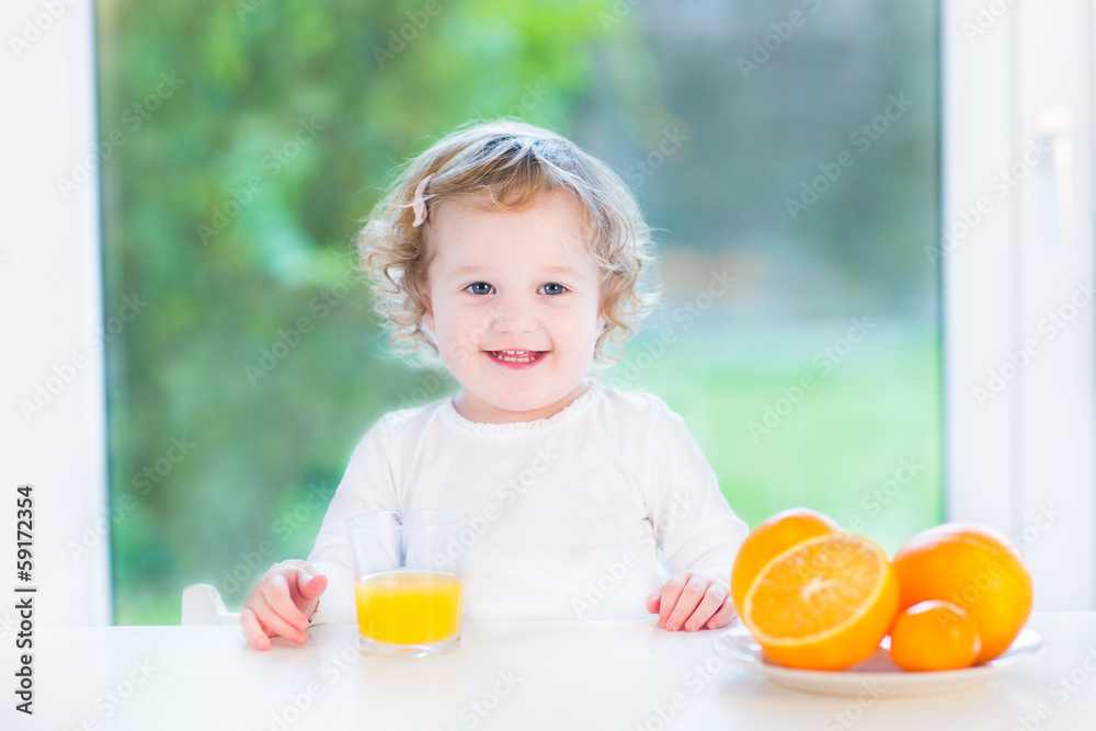 Girl having orange juice for breakfast sitting at a white table Girl having orange juice for breakfast sitting at a white table