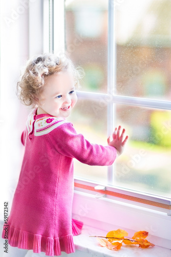 Laughing toddler girl watching out of the window in autumn