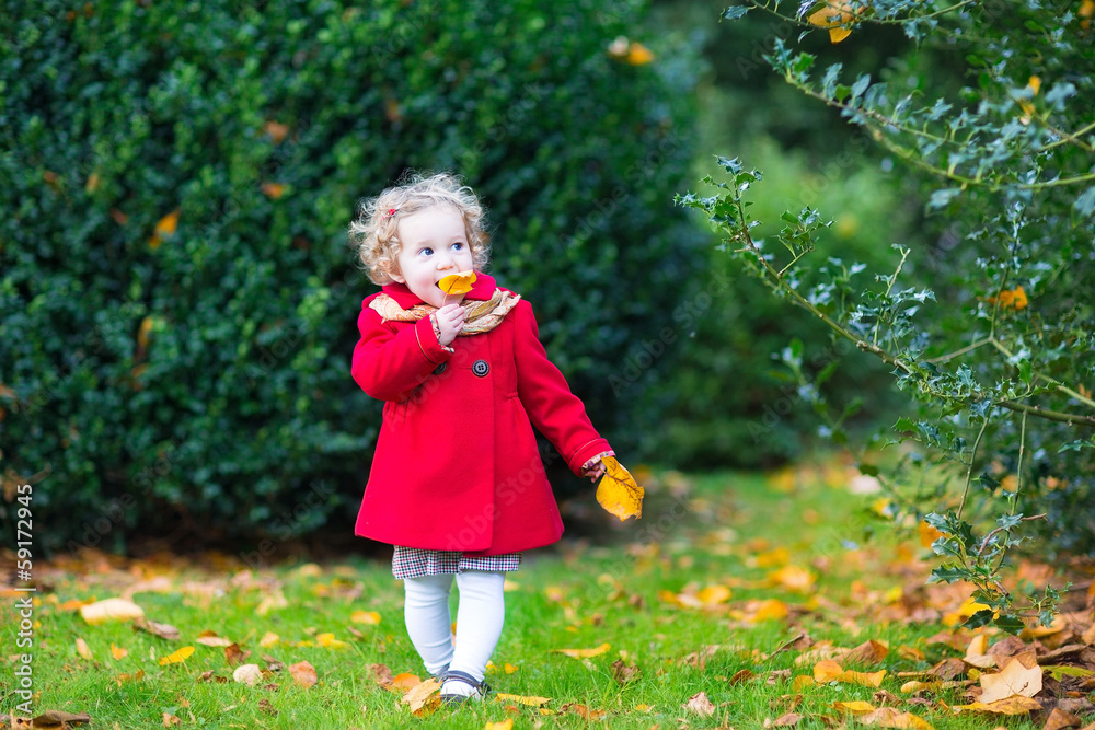 Cute toddler girl with curly hair wearing a red coat in a garden Cute toddler girl with curly hair wearing a red coat in a garden
