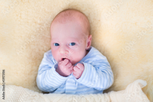Newborn baby with his hand in the mounth relaxing on a warm bed